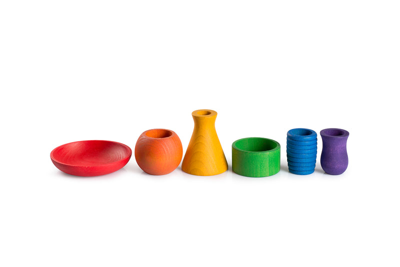 The image shows six colorful wooden objects arranged in a row. Each object is a different shape and color. From left to right, the objects are:

A red shallow bowl.

An orange rounded pot.

A yellow conical vase.

A green cylindrical ring.

A blue ribbed cylinder.

A purple vase-like object.

These objects are interesting because they demonstrate a variety of shapes and colors, which could be used for educational purposes, such as teaching children about colors, shapes, and sorting.